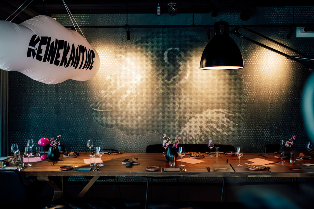 Langer gedeckter Holztisch in einer modernen Kantine mit dekorierten Sitzplätzen und großer Wandgestaltung mit Affen-Motiv im Hintergrund.